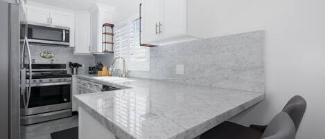 A modern kitchen with white cabinetry, a marble countertop, stainless steel appliances, and a built-in oven.