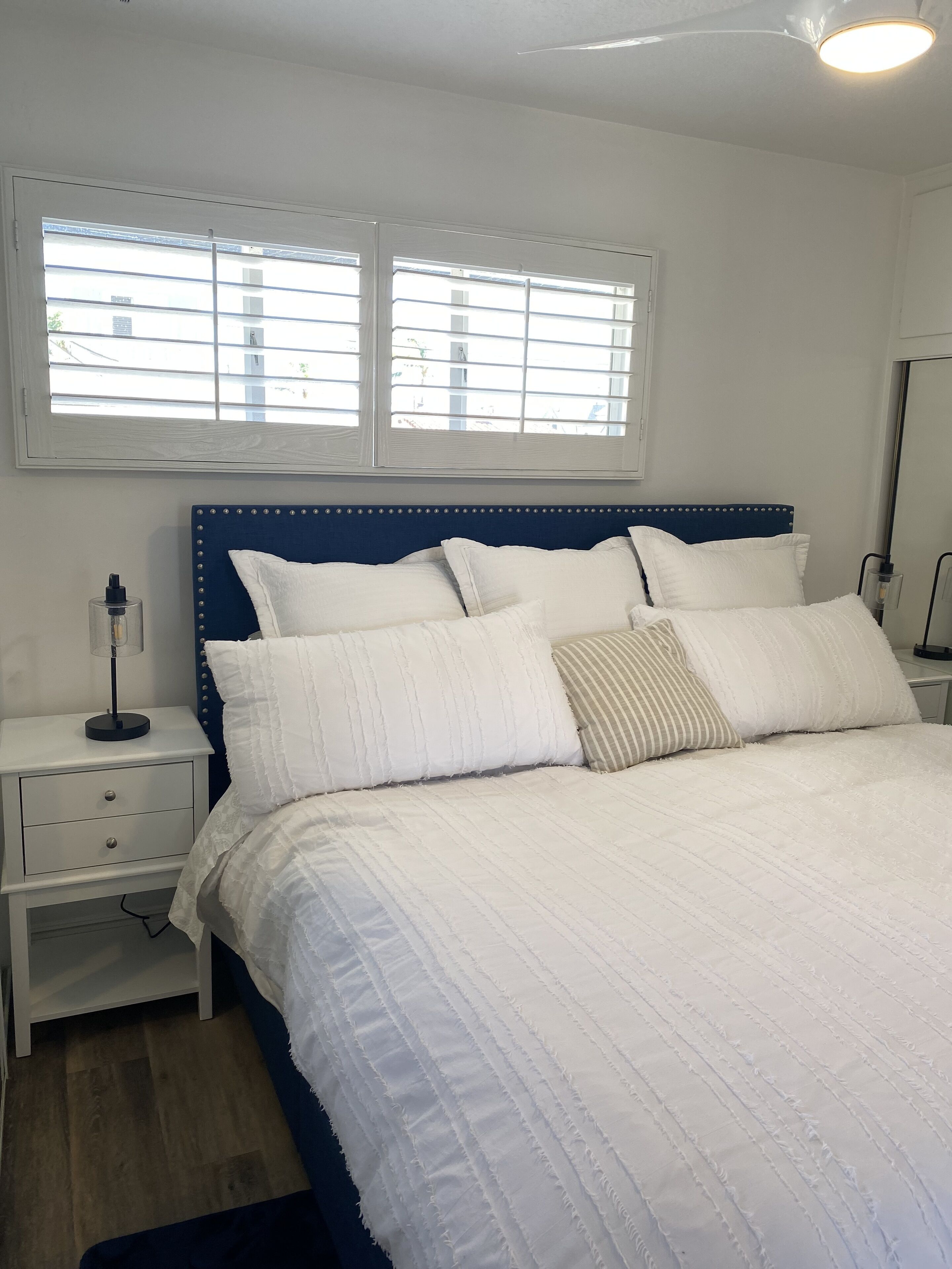 A neatly made bed with a blue headboard, white bedding, and a bedside table with a lamp.