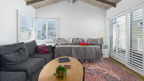 A modern living room with a gray sofa, a wooden coffee table, and a gray bed with patterned pillows. - 3 Properties From the Beach (Newport Beach)
