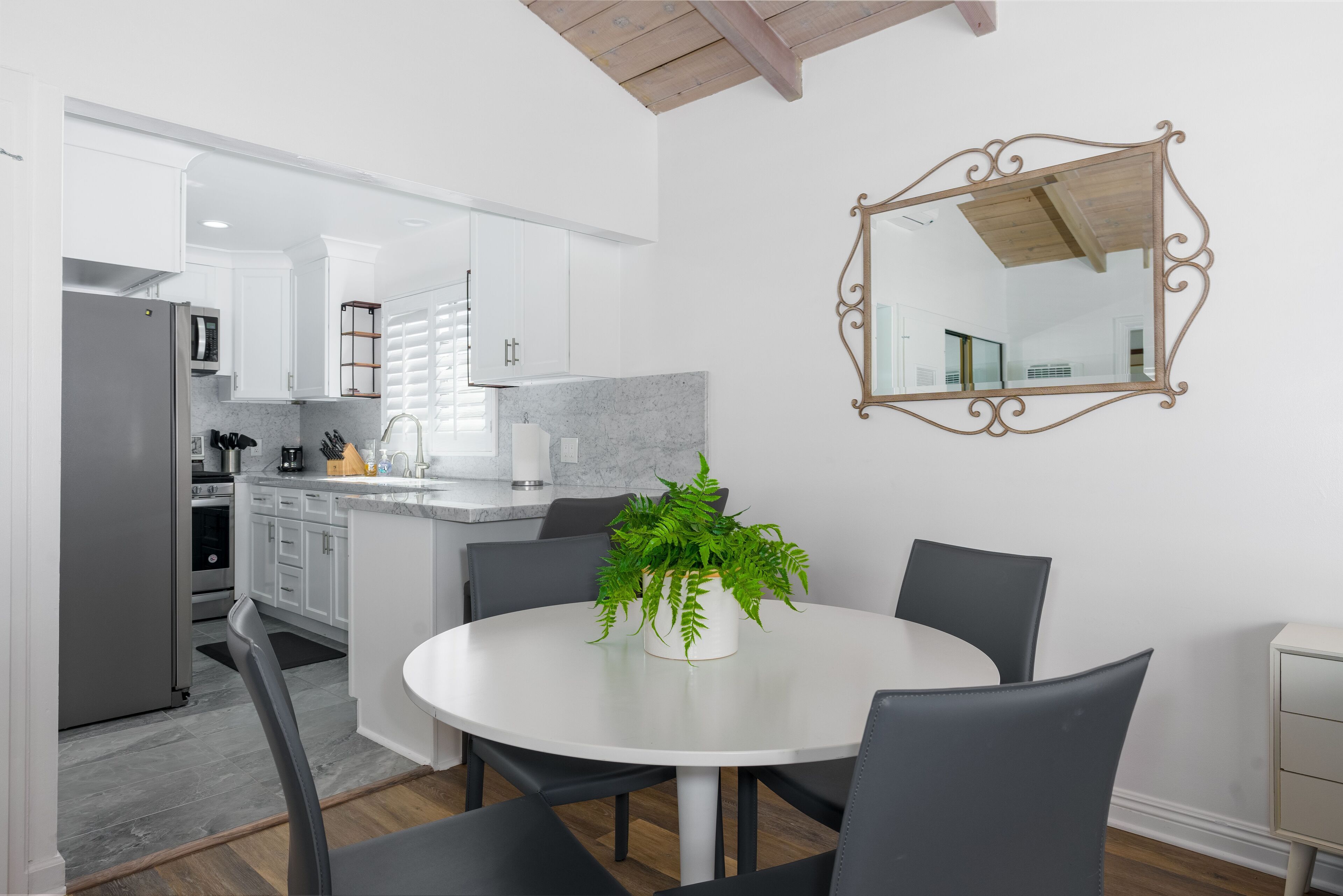 Una cocina moderna con armarios blancos, encimera de mármol y comedor con mesa y sillas blancas.