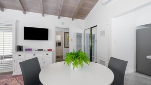 A modern dining area with a round table, two chairs, a potted plant, a flat-screen TV, and a white cabinet. - 3 Properties From the Beach (Newport Beach)