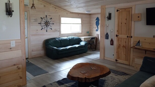 Et hyggeligt interiør i en hytte med træloft, en grøn sofa, et træbord og rustik indretning, inklusive et vægur og monterede padler.