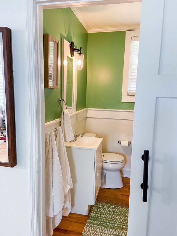 A bathroom with green walls, a white sink, a toilet, and a mirror with a towel hanging on the wall.