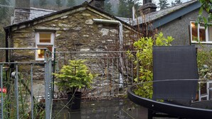 Ein Steinhaus mit einem kleinen Fenster, einem Metallzaun und einem Blumentopf im Vordergrund.
