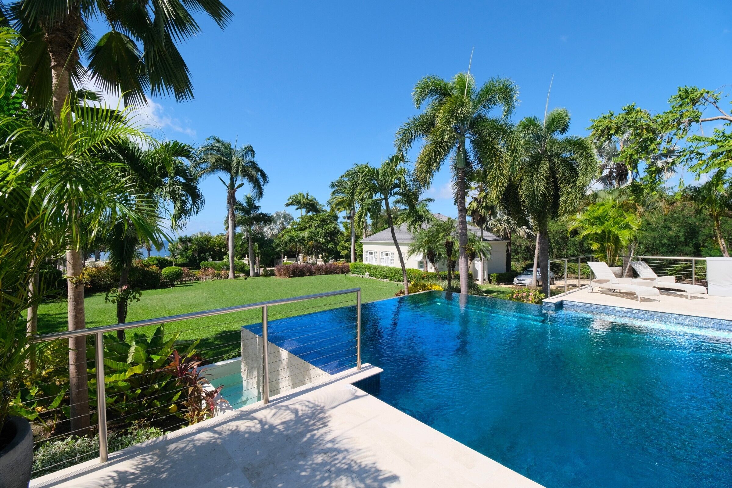 A swimming pool with a clear blue water, surrounded by palm trees and a well-maintained lawn.