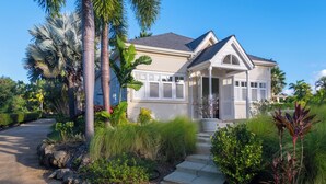 A two-story house with a covered porch, surrounded by tropical vegetation and a paved driveway. - The Garden Loft with pool and club house access (Mount Standfast, St. James)