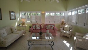 A living room with a pink sofa, white armchairs, a glass coffee table, and a ceiling fan. - The Garden Loft with pool and club house access (Mount Standfast, St. James)