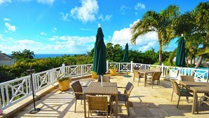 A patio area with outdoor furniture and umbrellas, overlooking a scenic view. - The Garden Loft with pool and club house access (Mount Standfast, St. James)