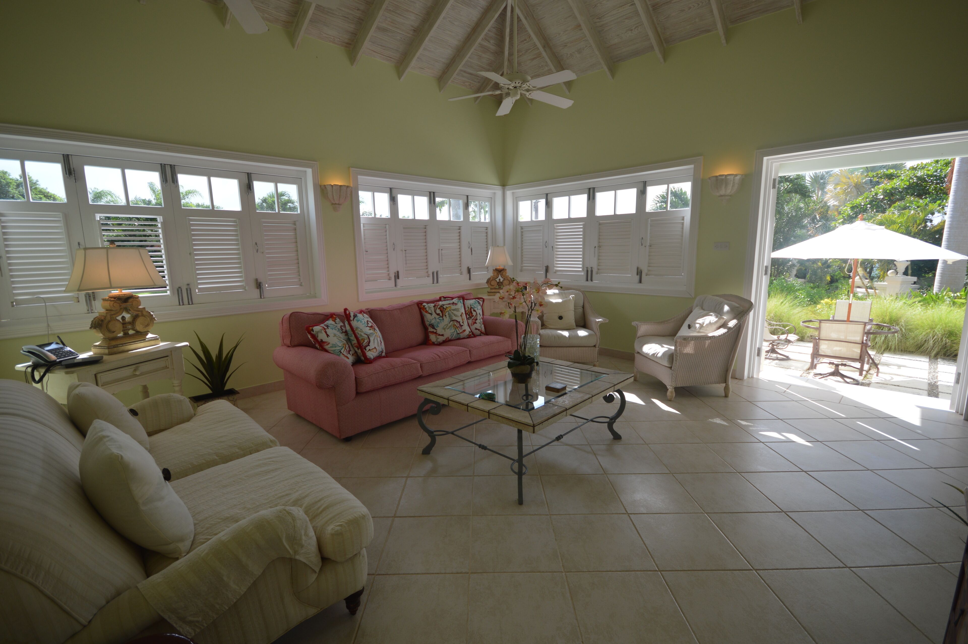 A spacious living room with a pink sofa, a glass coffee table, and a ceiling fan.