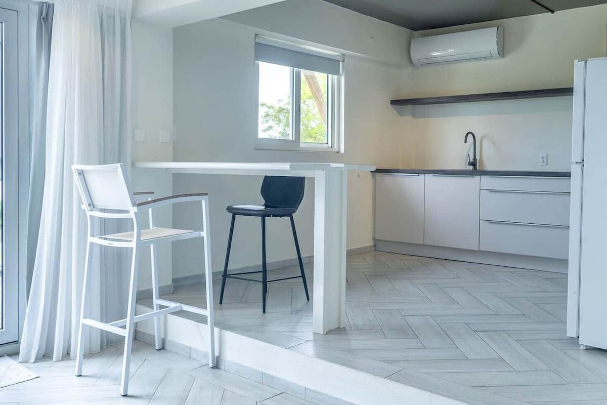 A modern kitchen with white cabinets, a white refrigerator, and a window with curtains.