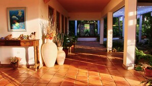 A hallway with tiled flooring, large vases with flowers, and a painting on the wall.