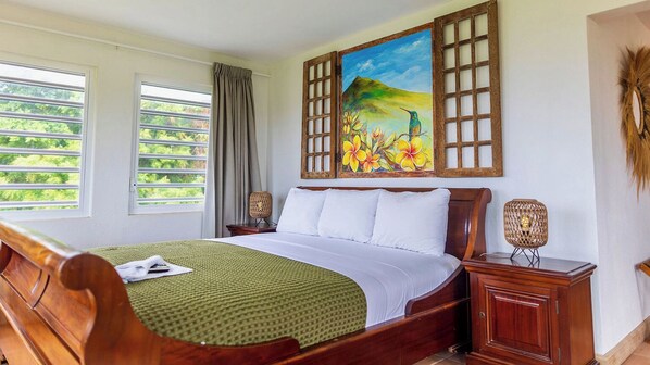 A neatly made bed with a green patterned bedspread, a wooden headboard, and white pillows. There is a painting of a tropical scene above the bed. -  Quill Gardens Boutique Hotel (Oranjestad)