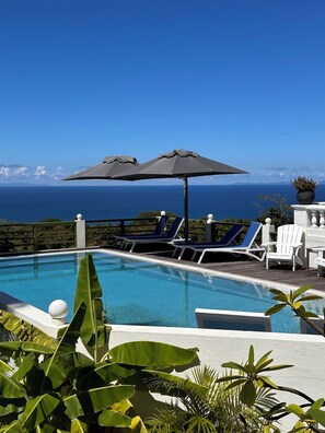 A pool with lounge chairs and umbrellas, overlooking a clear blue sea. -  Quill Gardens Boutique Hotel (Oranjestad)