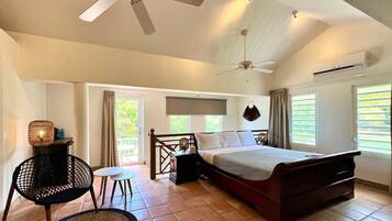 A bedroom with a bed, a ceiling fan, an air conditioning unit, and a view of greenery outside.