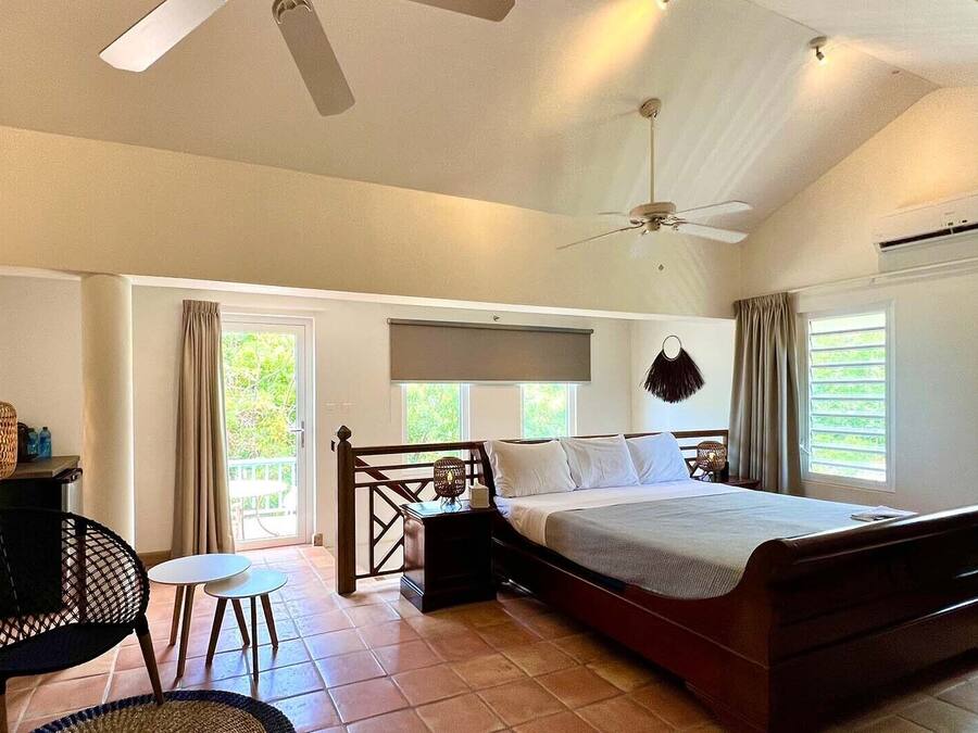 A bedroom with a bed, a ceiling fan, an air conditioning unit, and a view of greenery outside.