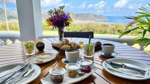 A breakfast table set with plates, cutlery, a vase of flowers, and a view of the ocean.