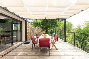 A wooden deck with a table and chairs, a large umbrella, and a view of greenery. - La Coursive: A Beautiful Luxury Home with a Pool (Montpellier)