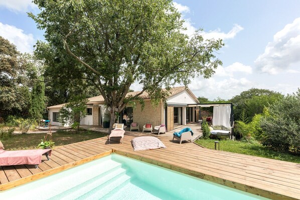 A wooden deck with a swimming pool, lounge chairs, and a covered seating area with cushions. - La Coursive: A Beautiful Luxury Home with a Pool (Montpellier)