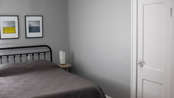 A bedroom with a bed, a white door, and two framed pictures on the wall.