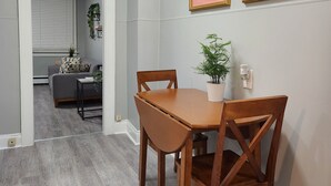 A dining area with a wooden table and chairs, a potted plant, and framed artwork on the wall. - Cozy & Comfy 1 Bedroom Apartment Downtown Sault, ON (Sault Ste. Marie)