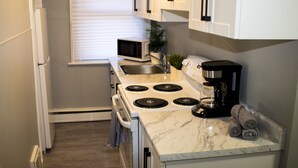 A compact kitchen with white cabinets, a built-in microwave, a stove, and a coffee maker. - Cozy & Comfy 1 Bedroom Apartment Downtown Sault, ON (Sault Ste. Marie)