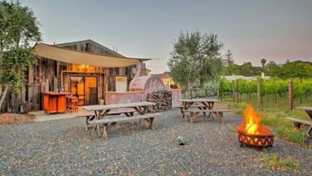 A rustic outdoor dining area with wooden tables and a fire pit.