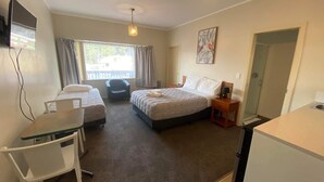 Een hotelkamer met twee bedden, een bureau, een stoel, een televisie en een raam met gordijnen.