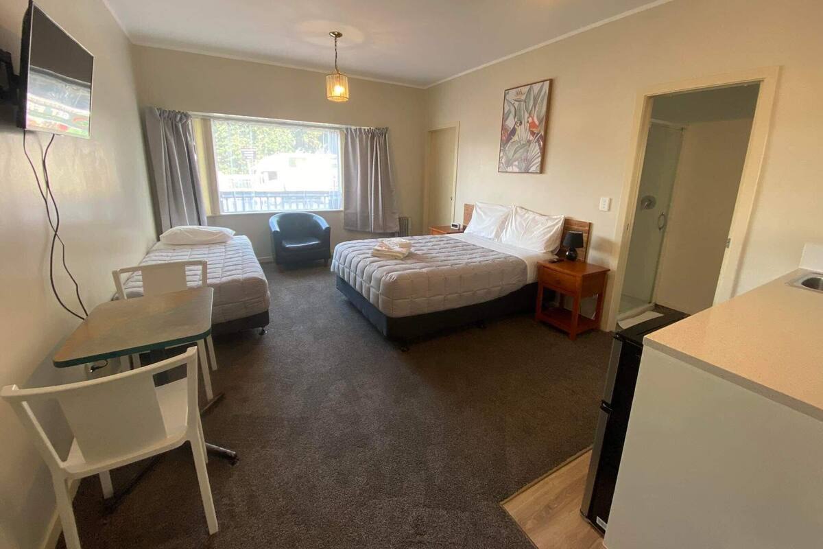 Une chambre d’hôtel avec deux lits, un bureau, une chaise, une télévision et une fenêtre avec des rideaux.