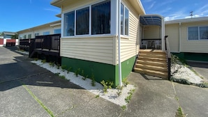 Een stacaravan met een groene basis en beige bekleding, een overdekte veranda en een kleine voortuin met wit grind en weinig gras.