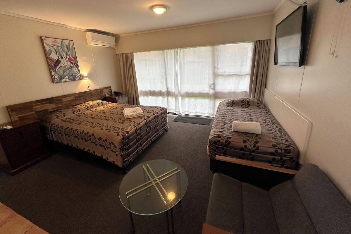 Une chambre d’hôtel avec un lit, un canapé, une petite table, une télévision et une fenêtre avec des rideaux.