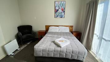 Quarto de hotel com cama, cadeira, mesa de cabeceira, radiador e janela com cortinas.