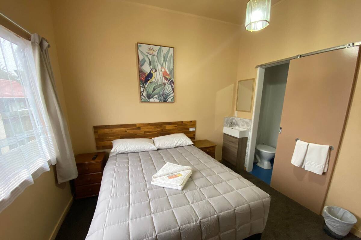 Une chambre à coucher comprenant un lit, une table de chevet, un tableau, une salle de bain avec un lavabo et des toilettes, ainsi qu’un porte-serviettes.