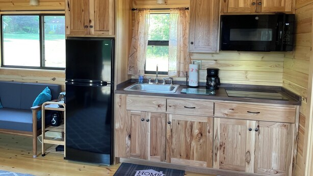 A compact kitchen with wooden cabinets, a black refrigerator, a microwave, and a coffee maker. - Cooperstown Double Play Hilltop Cabin B (Cooperstown)