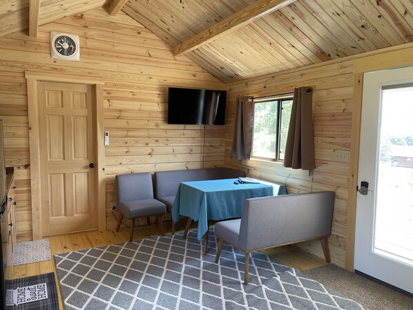 Ett mysigt stugrum med träpanel på väggarna, ett bord med stolar, en tv som är monterad på väggen och en dörr som leder ut.