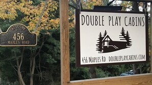 A sign for Double Play Cabins at 456 Maple Road, featuring a cabin illustration and the website address. - Cooperstown Double Play Hilltop Cabin B (Cooperstown)