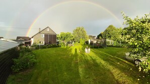 A residential backyard with a house, a trampoline, and a visible rainbow.