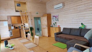 A cozy cabin interior with wooden walls, a kitchenette, a dining area, and a living room with a couch and chairs.