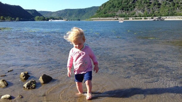 A child standing in shallow water near rocks.