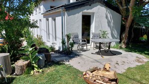 A small house with a patio, a table, and chairs. There is a fire pit with wood in the foreground.