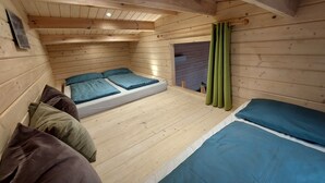 A cozy wooden cabin room with a loft bed, a lower bunk bed, and a small enclosed space with a window.