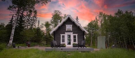 A cabin with a porch, surrounded by trees and a grassy area.