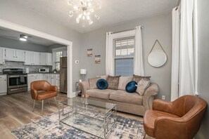 Un salon avec un canapé, deux fauteuils, une table basse et, au fond, une cuisine.