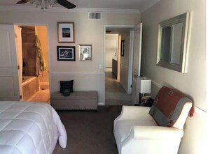 Two beds with white bedding, a comfortable armchair, and a bench create a cozy space.