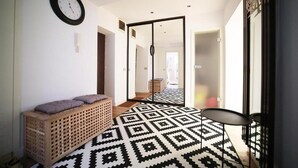 Un pasillo con suelo estampado, un banco, un reloj de pared y una puerta corredera que da a otra habitación.
