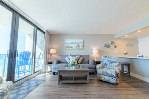 Relax in this stylish living room with a sofa, armchair, and coffee table, plus a balcony with a sliding glass door.