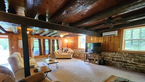 A cozy cabin interior with a stone fireplace, wooden ceiling beams, and a comfortable seating area. - Charming re-imagined bank barn cabin. (Millmont)