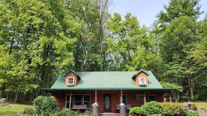 A wooden cabin with a green roof, surrounded by lush greenery and trees. - Charming re-imagined bank barn cabin. (Millmont)