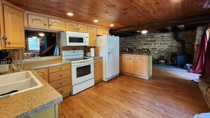 A kitchen with wooden cabinets, a stove, microwave, and refrigerator. - Charming re-imagined bank barn cabin. (Millmont)
