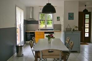 A kitchen with a dining table, chairs, a hanging light fixture, a window, and a door. - Pipa - Sarzeau - Gîte (SARZEAU)