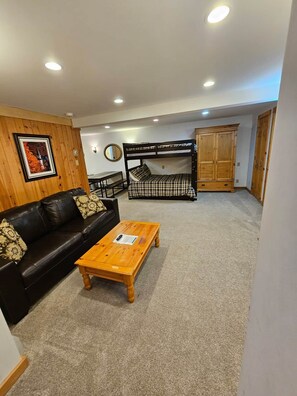 A furnished living room with a black leather sofa, a wooden coffee table, a bunk bed, and a wooden wardrobe. - Ski-in/Ski-out Studio on Okemo Sachem Trail (Ludlow)